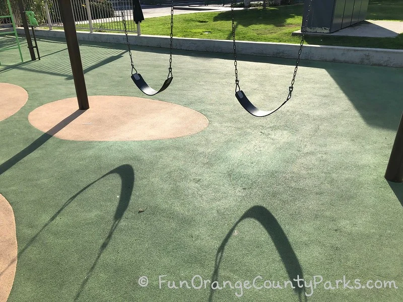 bench swings in sun with shadow on playground