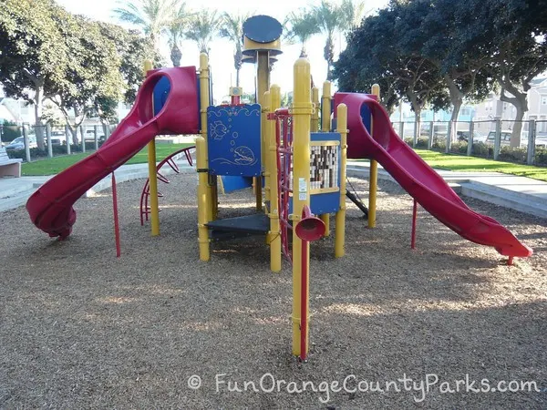 38th Street Park playground with red slides on either side with yellow and blue on a bark play surface