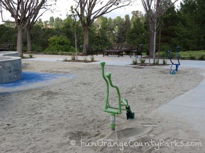 blue and green diggers in a sand play area at Pavion Park with trees and seating area in the background