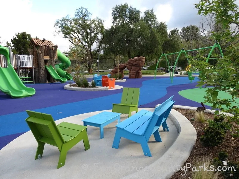 blue bench and table with 2 green chairs with view of playground and rock climbing structure in the middle of Pavion Park in Mission Viejo