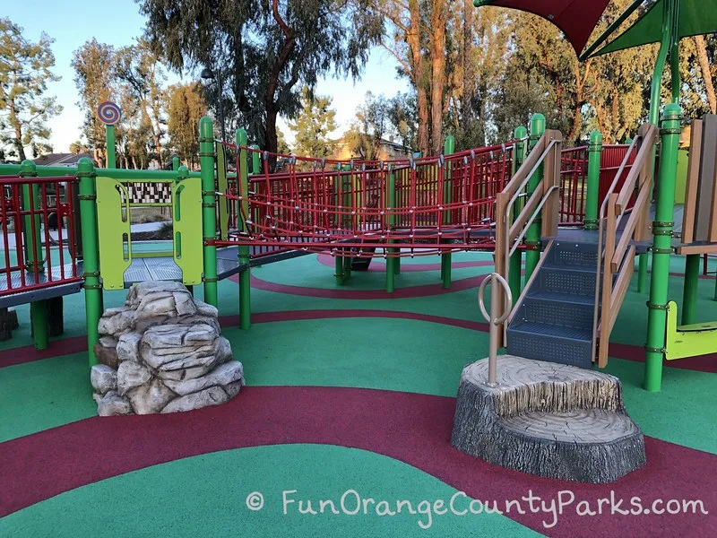 rope bridge with boulder climber on left and log shaped stairs on right