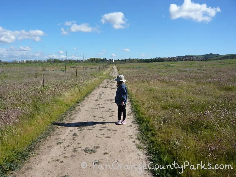 Quail Hill Loop Trail with girl wearing jeans and hat surrounded by green grass and blue sky