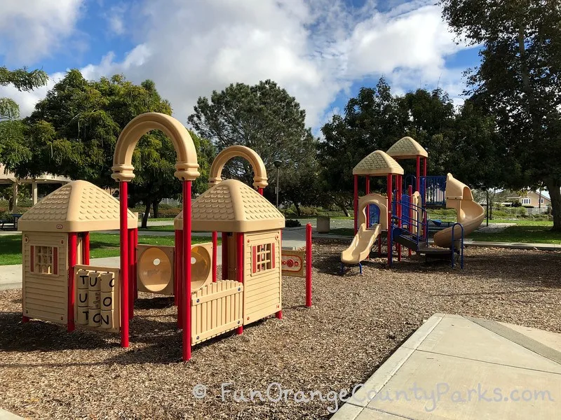 Toddler size playground at Ocean Breeze Park. Older play equipment than the rest of the playground. Short slides and clubhouse for pretend play on bark surface.