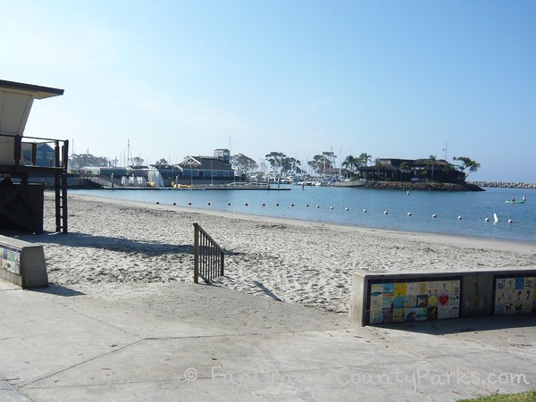 Baby Beach pedestrian entrance from concrete to sand with swimming area and harbor in the background