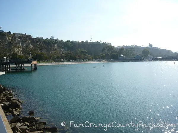 View of Baby Beach at Dana Point Harbor with ocean in foreground and a thin strand of beach along bluffs