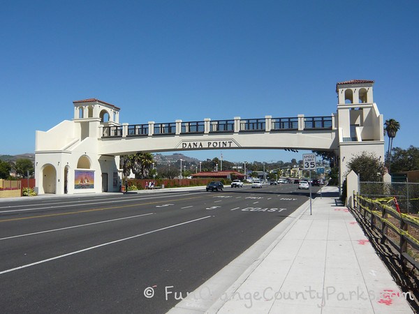 Spanish style walking bridge over Coast Highway near Dana Point Harbor. "Dana Point" written on the bridge and Coast Hwy writen on street.