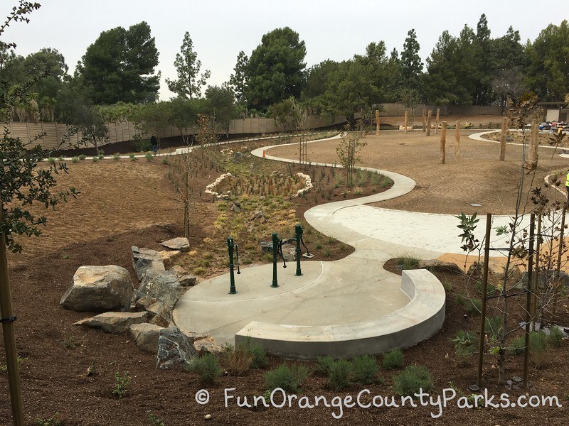 empty playground with dirt patches and concrete pad with water pumps in foreground