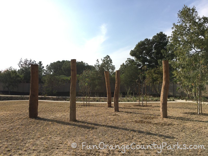 Irvine Adventure Playground area with 5 large tree trunks planted upright in a barren field