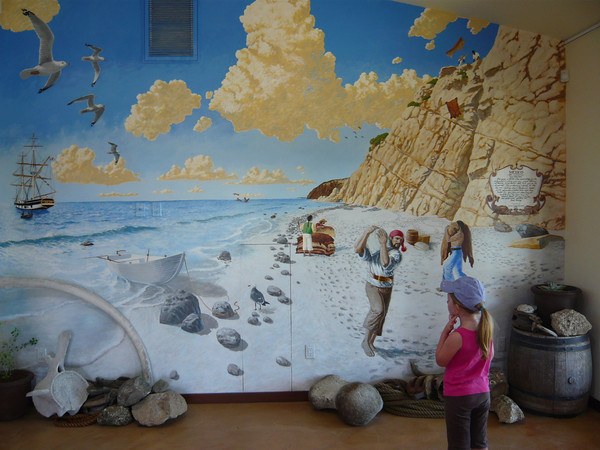 young girl with a pink shirt and purple cap looking at mural of pirates on the beach below the bluff at Dana Point Headlands