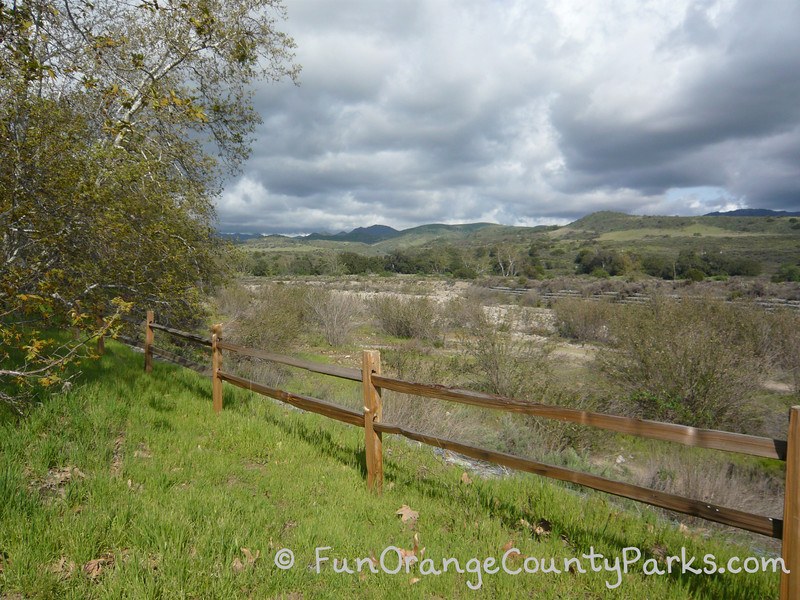 caspers wilderness park with wooden fence on green grass with storm clouds over green hills in the distance