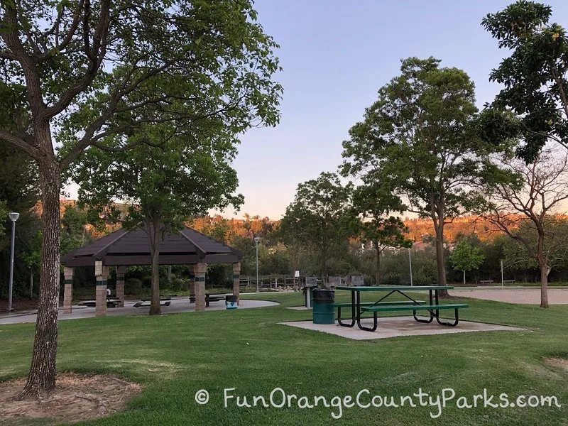 covered picnic shelter and open air picnic table on a grassy area with trees at Ronald Reagan Park in Anaheim Hills