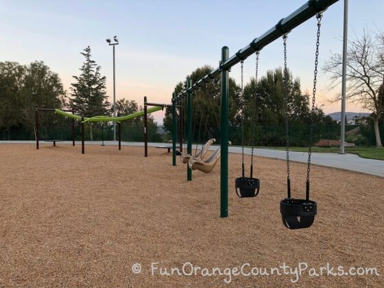 2 baby swings, 2 accessible swings, 2 bench swings, and a zip track on a bark play surface at Ronald Reagan Park in Anaheim Hills