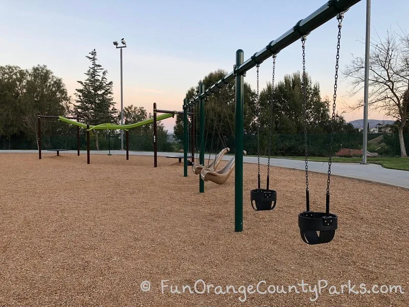2 baby swings, 2 accessible swings, 2 bench swings, and a zip track on a bark play surface at Ronald Reagan Park in Anaheim Hills