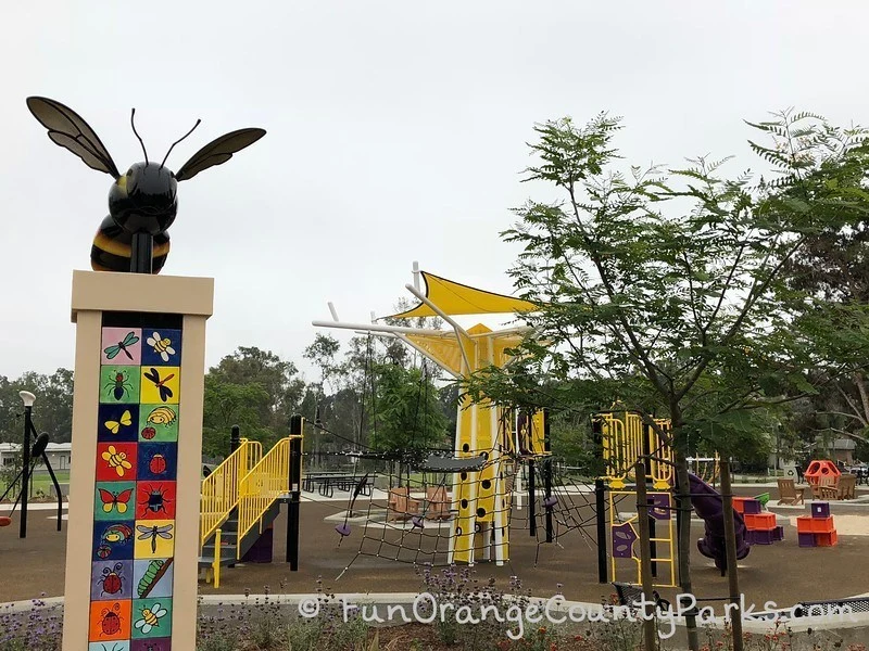 bumble bee sculpture on top of a colorful tiled pedestal with the bright yellow playground in the background