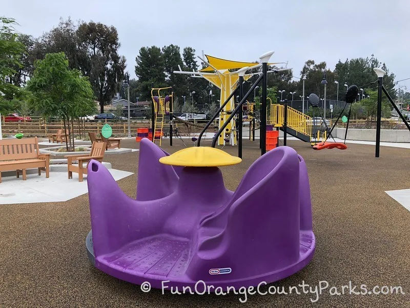 plastic purple merry-go-round at Cordova Park in Mission Viejo with playground in view behind it