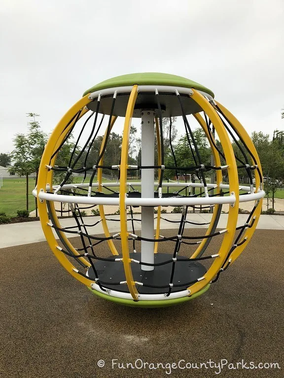 large yellow globe-shaped equipment with black netting tall enough for kids to stand inside while it spins