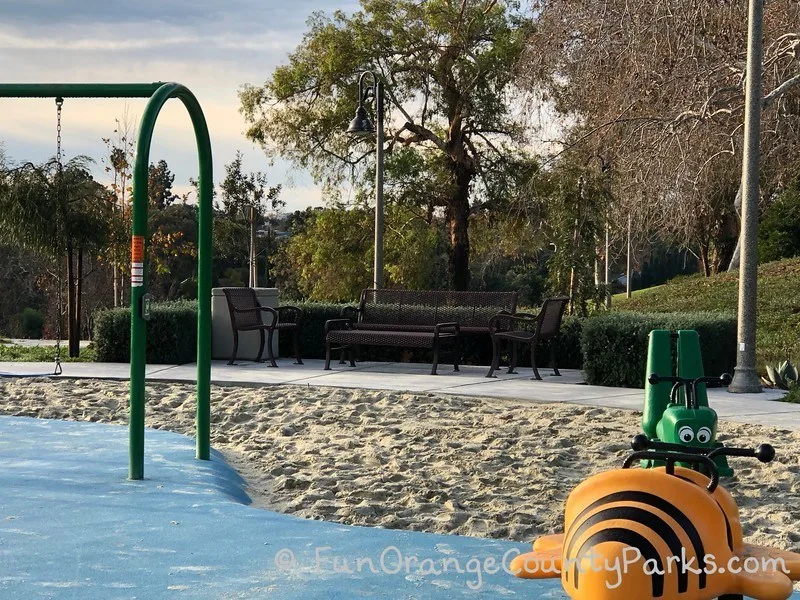 bench area near the swings for parents with ride on spring toys shaped like a bumblebee and grasshopper