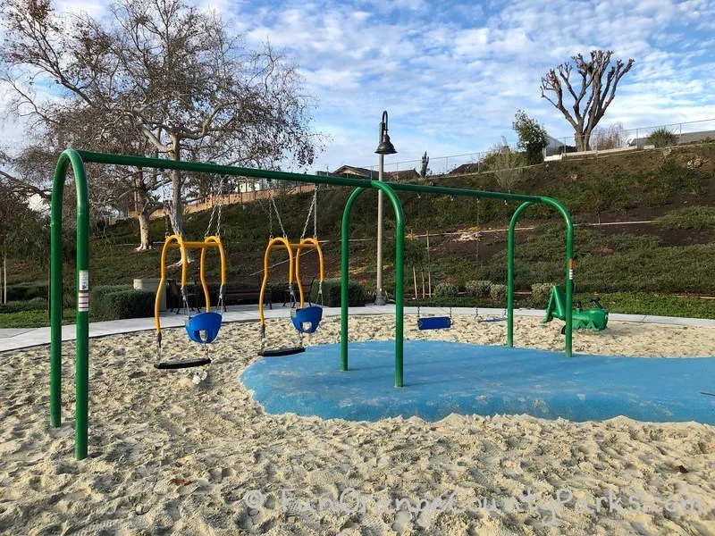 two mommy and me swings and two bench swings over sand and a recycled rubber surface