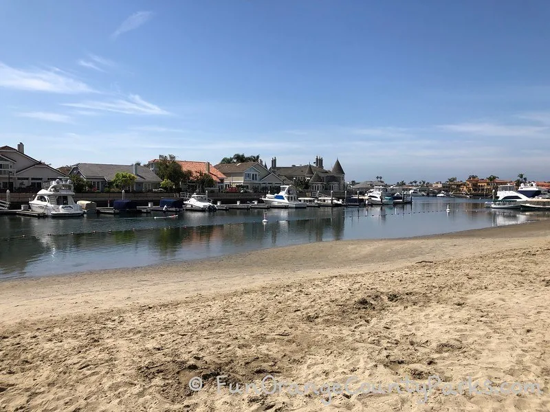 beach at Seabridge Park with sand in foreground and houses with boats parked in background inside harbor