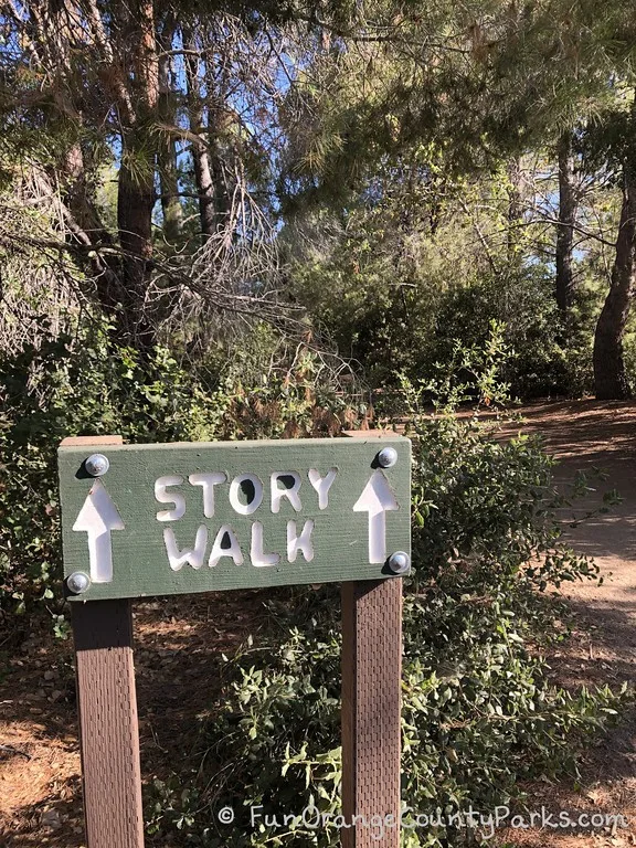 Story Walk sign with white words carved into green wood with trees as background