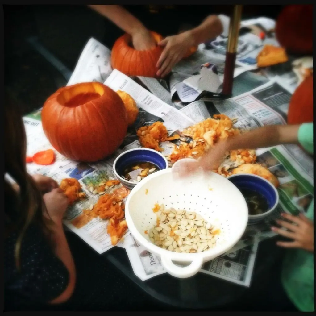 school age children carving October Halloween pumpkins with bowls of pumpkin seeds on newspaper