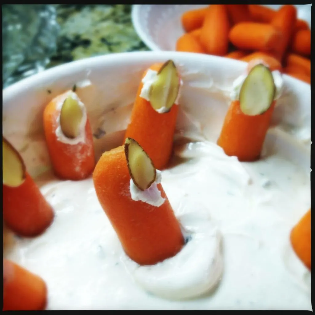 carrots in a white dip with almonds to make them look like witch's fingernails