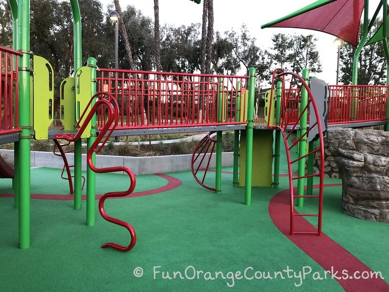 cherry park lake forest playground with red bridge and 4 different ladders visible on a green recycled rubber play surface