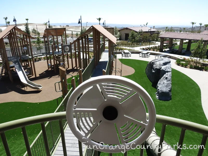 view of Baker Ranch Community Park from the top of the play structure near with the ocean visible in the distance and a large climbable rock on the playground