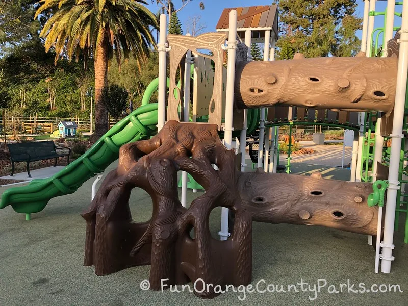 two tree tunnels and tree root climber on playground with neon green slide leading off the left side of the photo