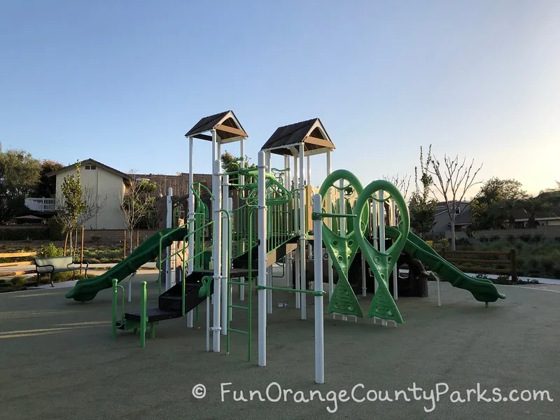 neon green playground with monkey bars and slides coming off either end on recycled rubber play surface at christopher park in mission viejo