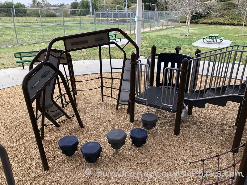 pedestals and clmibing apparatus on the playground at Fullerton Sports Complex with picnic tables and lawn area in the background