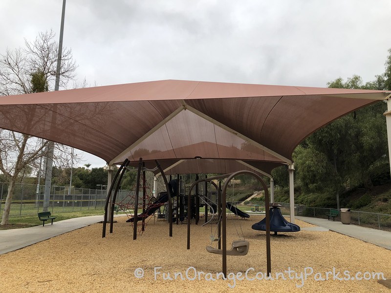 large brown shade cover over playground with cloudy skies