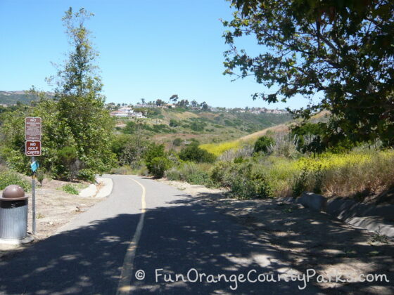 paved trail leading to Salt Creek Trail in Dana Point with brush and trees surrounding the trail