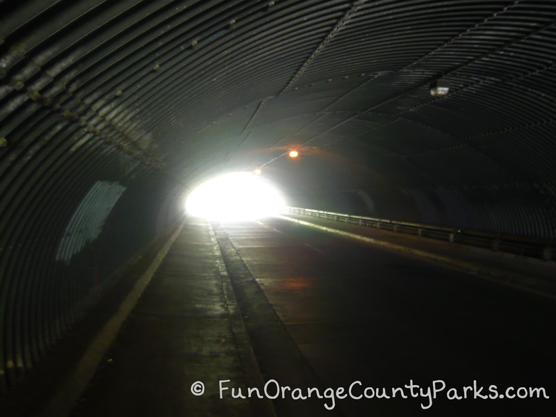 a dark metal tunnel with a bright light at the end and sidewalks