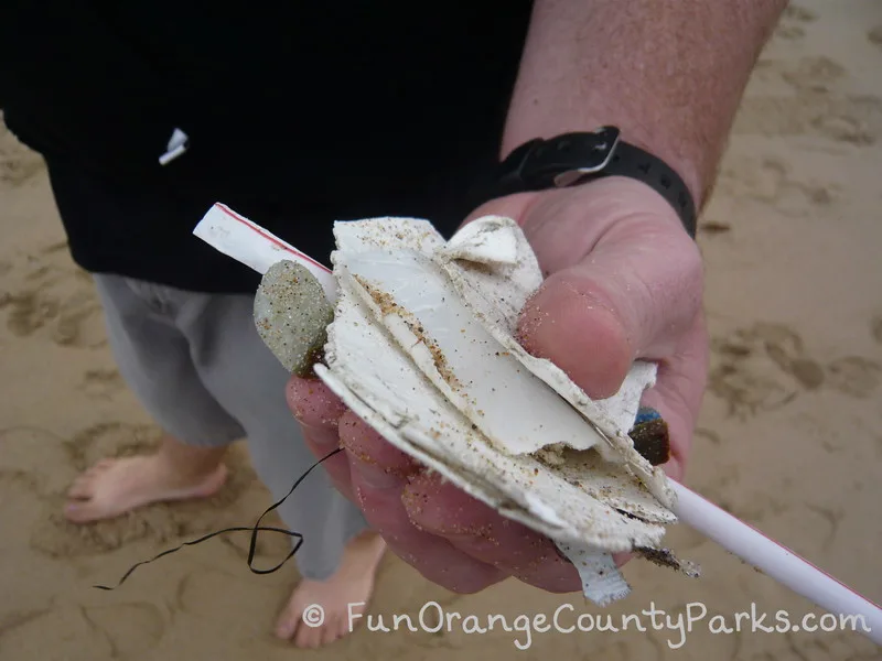 hand holding a handful of beach trash with bare feet and shorts beneath the hand