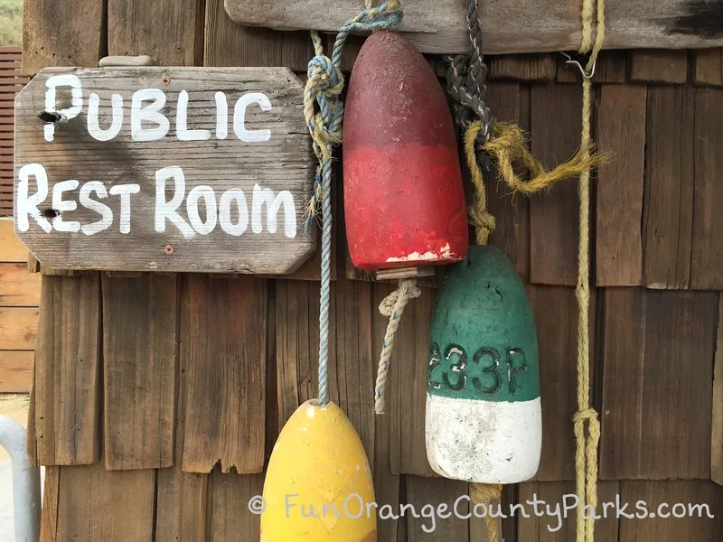 public restroom sign with colorful buoys hanging on a shingled wall