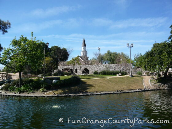 view across the moat of heritage park play island in cerritos where you can see the church tower and colonial style wall against a blue sky