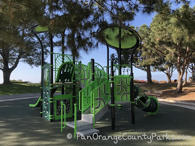 neon green and black playground with circular sun shades and modern feel surrounded by pine trees at Lantern Bay Park in Dana Point