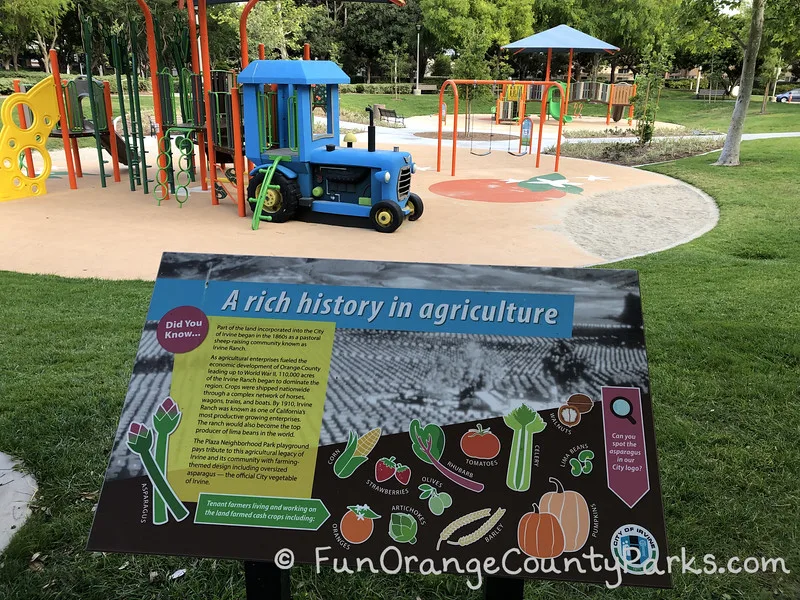 Plaza Park sign about "A rich history in agriculture" in the foreground with a blue tractor built into a play structure with 2 bench swings and another play structure visible