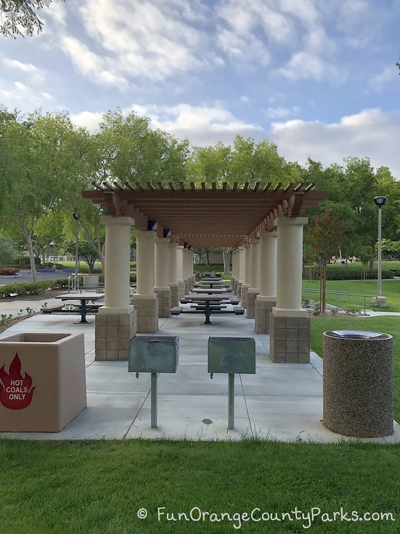 covered picnic area with lots of 4-person tables that have built-in benches. 2 grills, a hot coals bin and a trash bin at either end