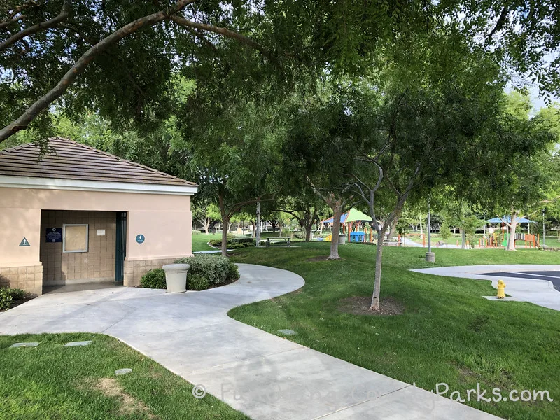 restroom building at Plaza Park in Irvine with a perspective that shows how close the playground is through the trees.