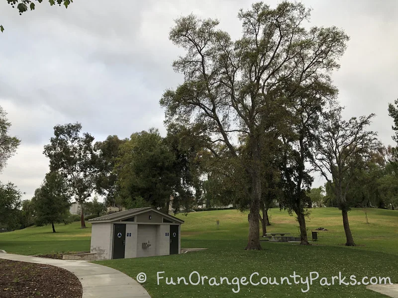 restroom building at Rolling Hills Park in Fullerton underneath tall trees against a cloudy sky