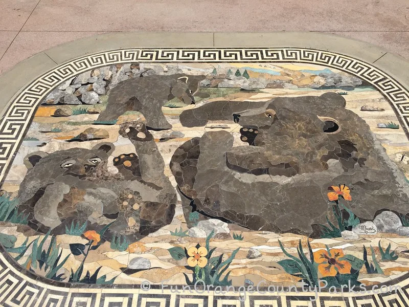 mosaic tile art set into concrete at the entrance to the playground featuring a family of bears playing in the forest and among the rocks