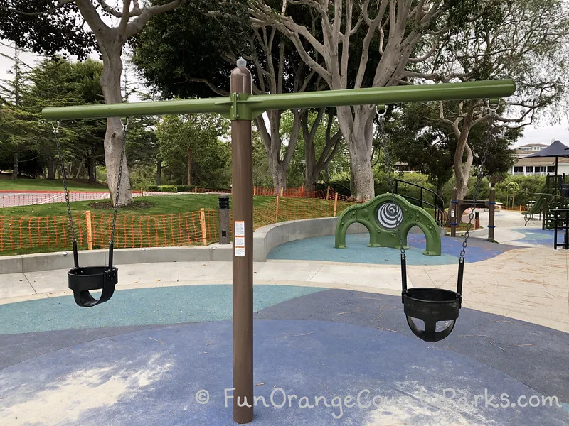 2 baby swings on blue recycled rubber play surface with trees in the background