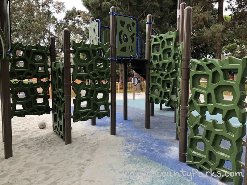 green playground panels that has holes in strange geometric shapes so children can climb across them using the holes as footholds
