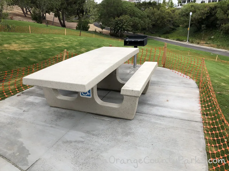 concrete picnic table with handicap sign underneath and grill at the top of a grassy hill