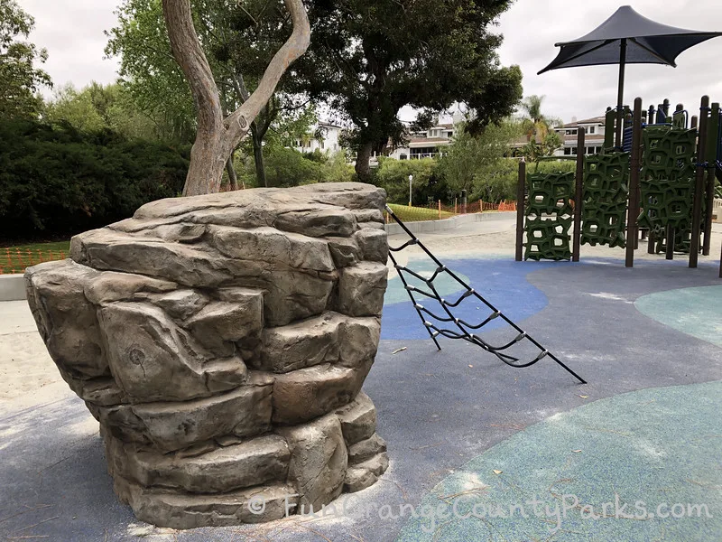 fake rock climbing structure with black rope grid for climbing and trees in background