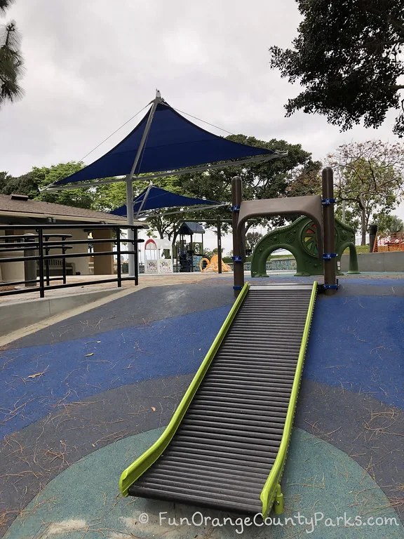 roller slide on a hill with blue shades and small playground at Grant Howald Park in Newport Beach in the background