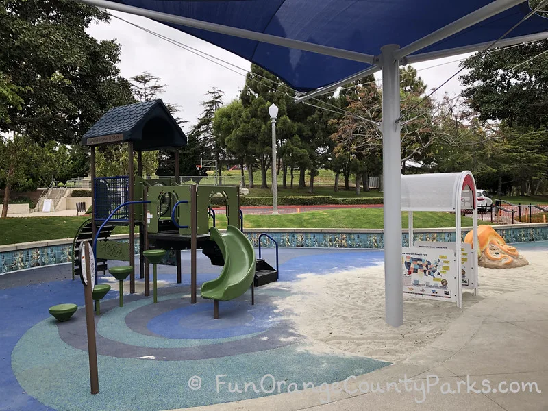 small playground with slide under blue shade cover on blue recycled rubber surface