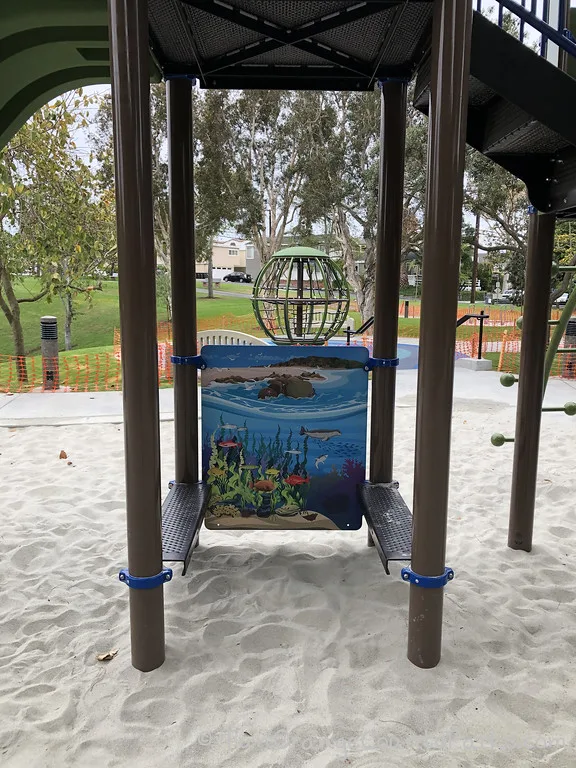 view of playground from under the slide to a seating area near ocean art and a spinning globe play equipment in the background